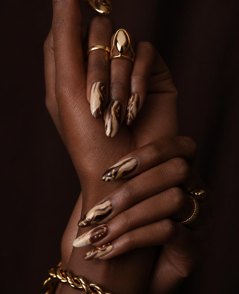 Hands with intricate cream-and-gold abstract nail art and bold gold rings