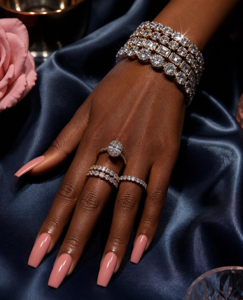 Hand with glossy pink nails, diamond rings and a diamond bracelet on navy satin